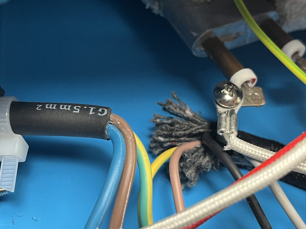 Close-up inside the ST-750 cabinet showing frayed gray fibrous material among electrical conductors near the boiler, with brown, blue, green-and-yellow, black, and heat-resistant braided wiring visible.
