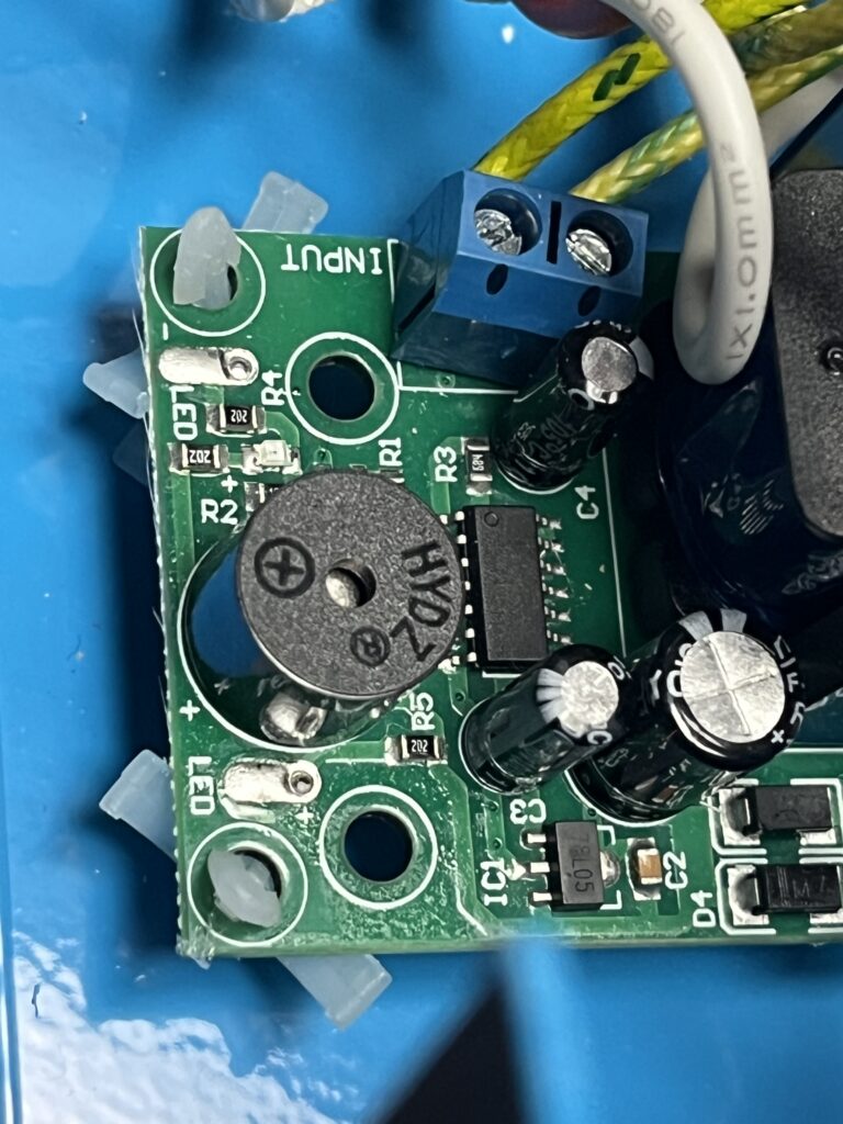 Close-up of the opposite end of the ST-750 HB-BJ-1 electronic board showing a round piezoelectric buzzer, integrated circuit, electrolytic capacitors, indicator LEDs, resistors, diodes, and input terminal connections.