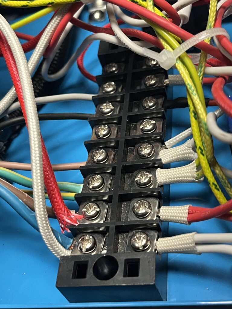 Close-up of the ST-750 internal barrier terminal strip showing multiple screw terminals and connected red, white, black, brown, blue, green-yellow, and heat-resistant sleeved conductors