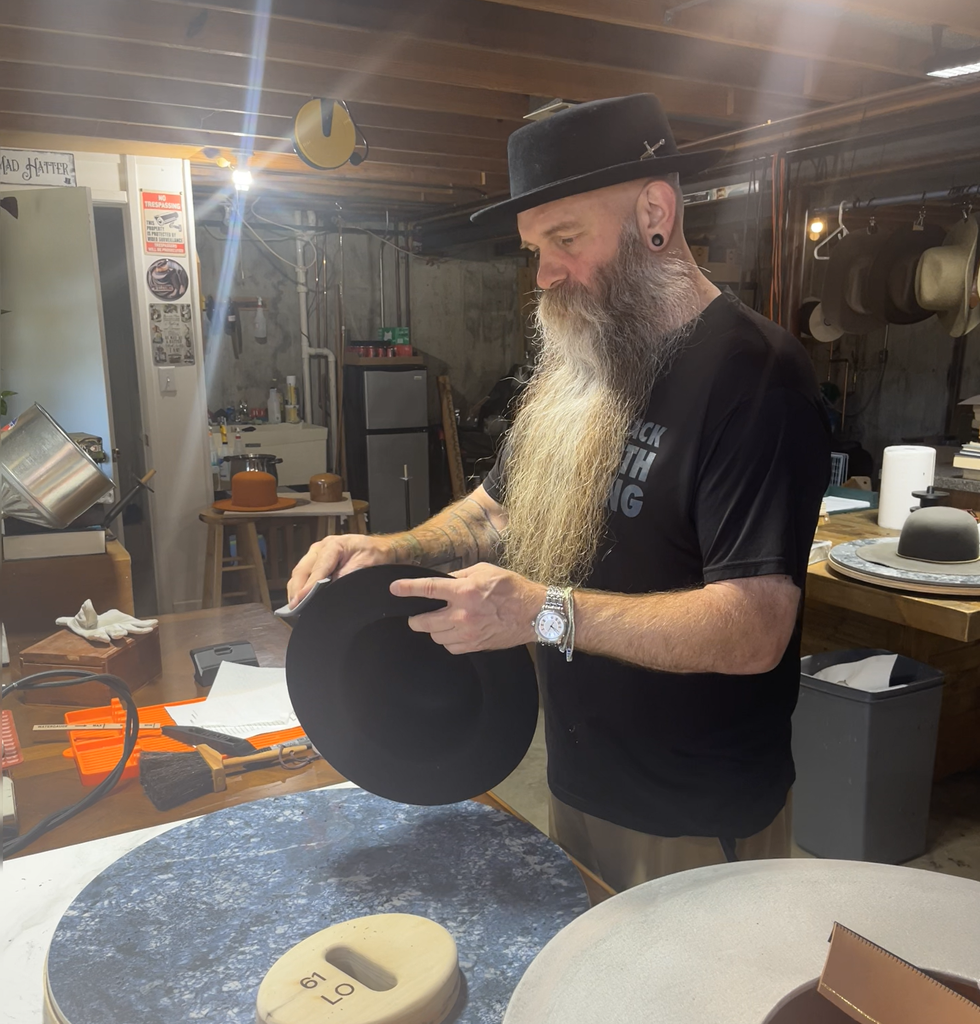 Sanding and refining the cut brim edge of the black 100% rabbit felt hat during construction of Project PM-26-010.