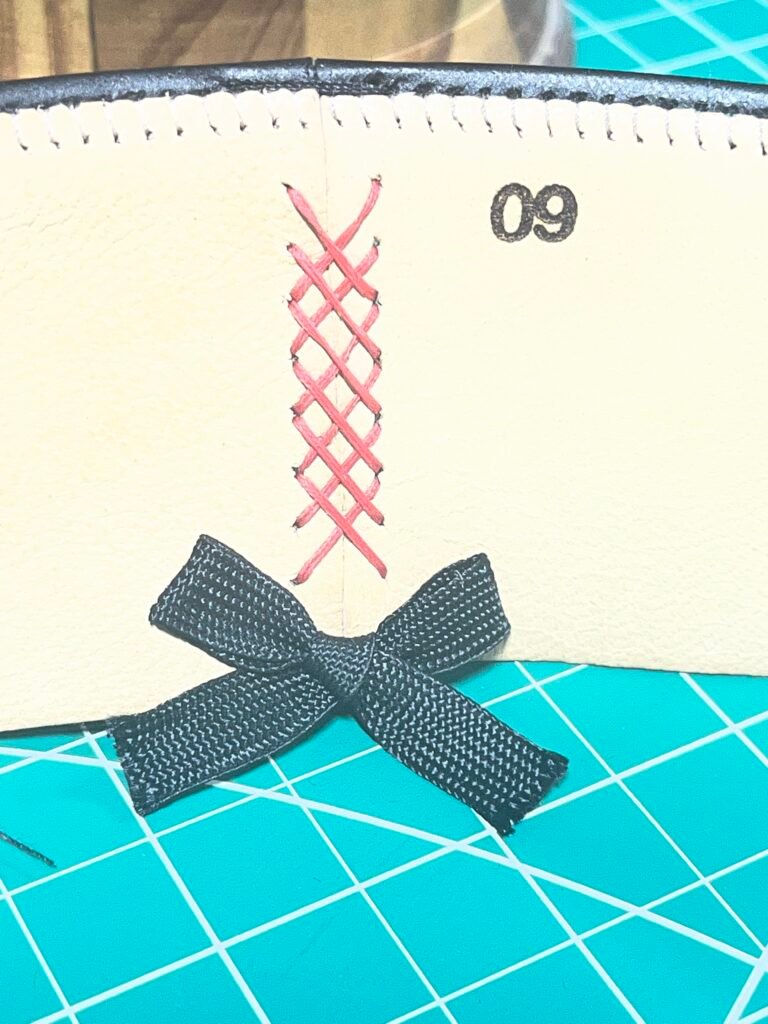 Prepared leather sweatband for Project PM-26-010 showing the joined seam, red decorative cross-stitching, and black bow.