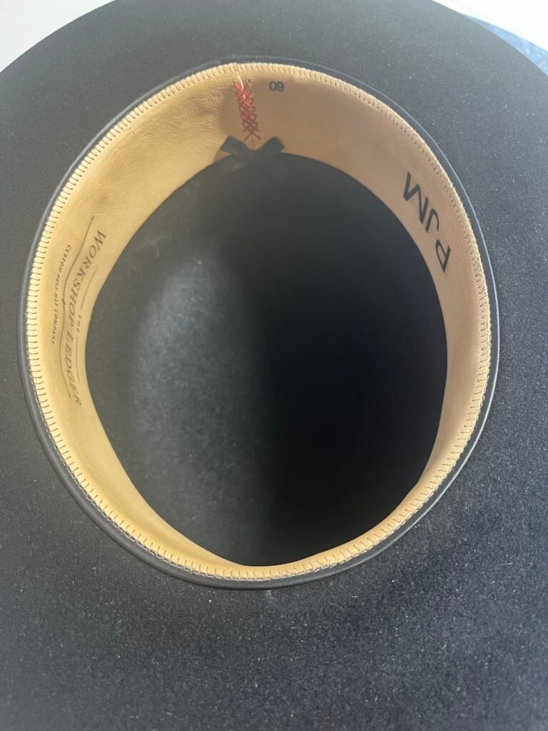 Installed leather sweatband inside Project PM-26-010 showing The Workshop Ledger branding, decorative seam, bow, and size markings.