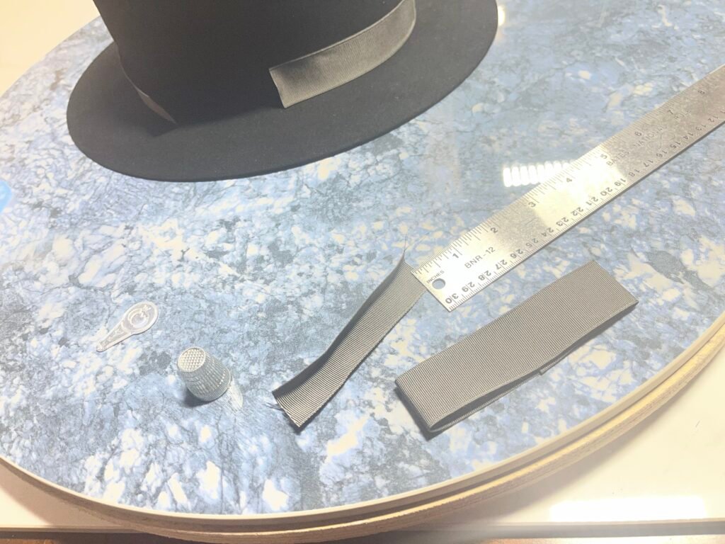 Measuring and preparing the gray grosgrain ribbon and bow for the black rabbit felt hat, Project PM-26-010.
