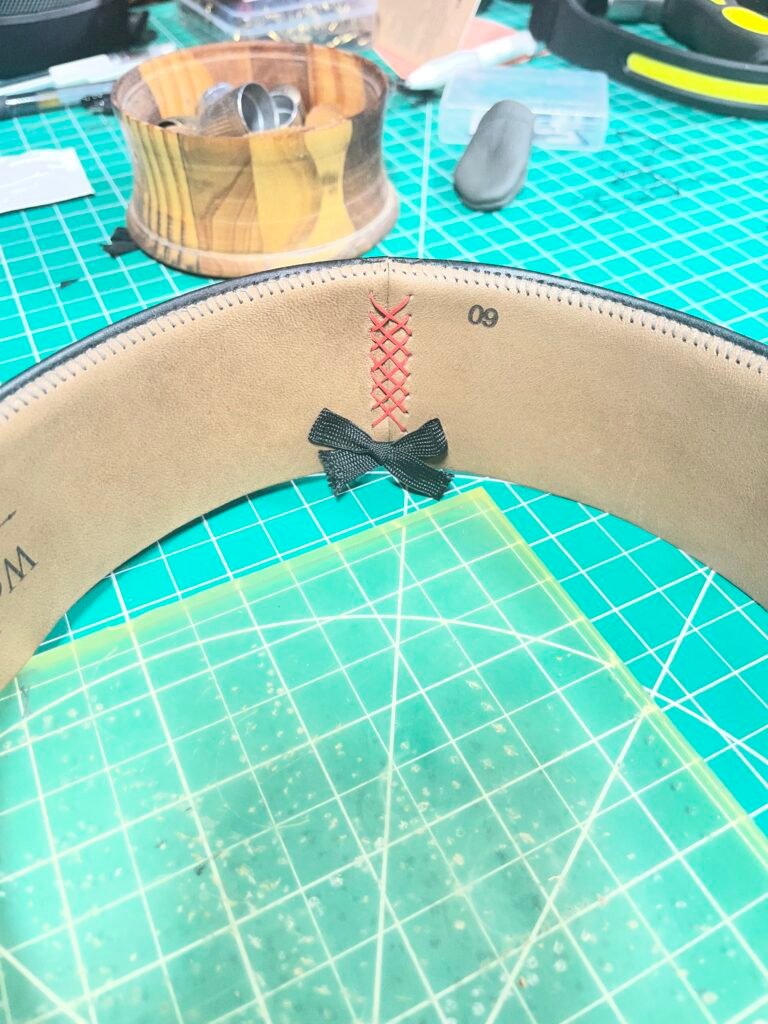 Prepared leather sweatband for Project PM-26-011 showing the joined seam, decorative cross-stitching, and sweatband bow.