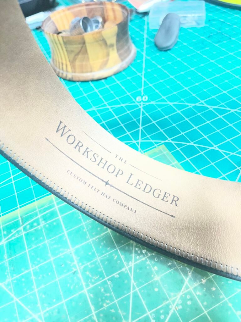 Prepared leather sweatband for Project PM-26-011 showing The Workshop Ledger branding before installation.