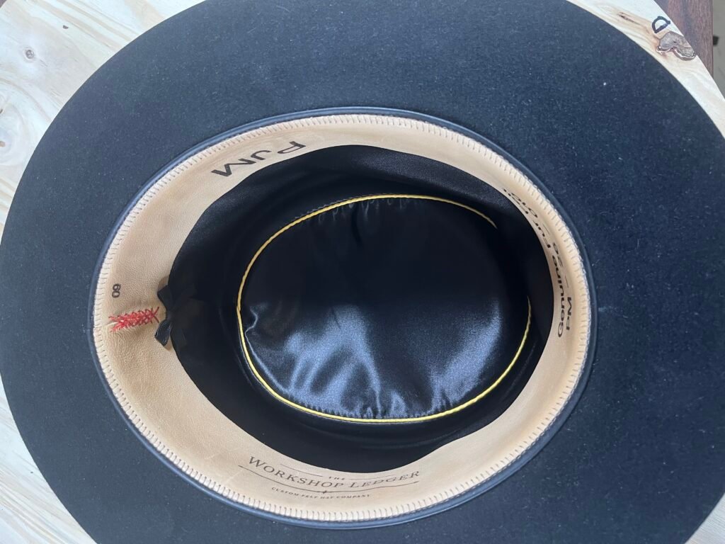 Interior of Project PM-26-010 showing the leather sweatband, black satin liner with gold piping, and finished interior details.