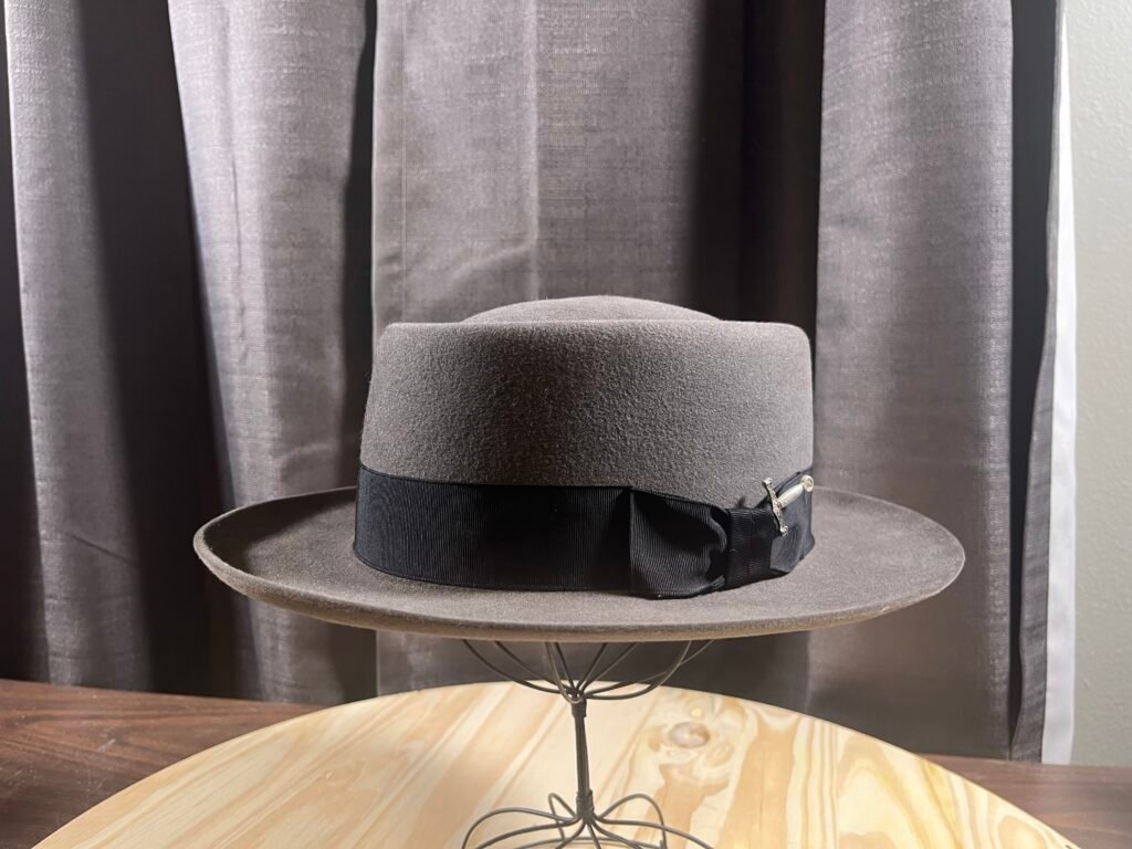 Finished gray 100% beaver felt pork pie hat with black ribbon and bow, Project PM-26-011, made at the Walton hat-making workshop.