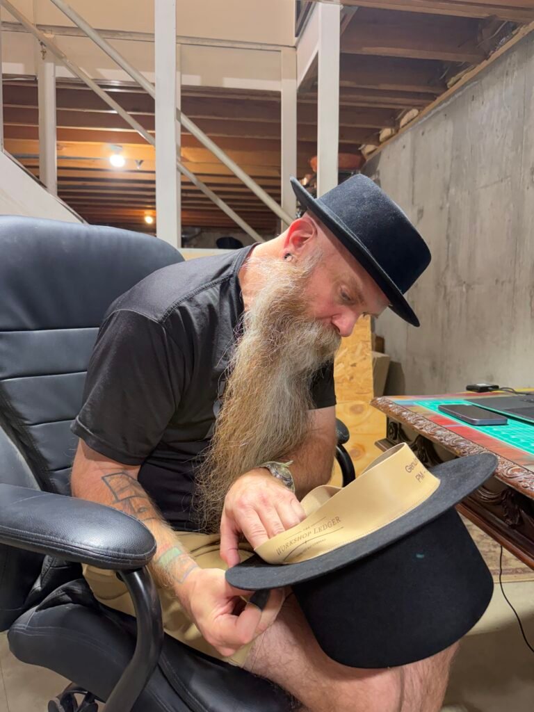 Hand installing the prepared leather sweatband into the black rabbit felt hat for Project PM-26-010.